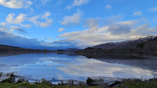 View over icy Loch Alviej with blue skies and some fluffy clouds