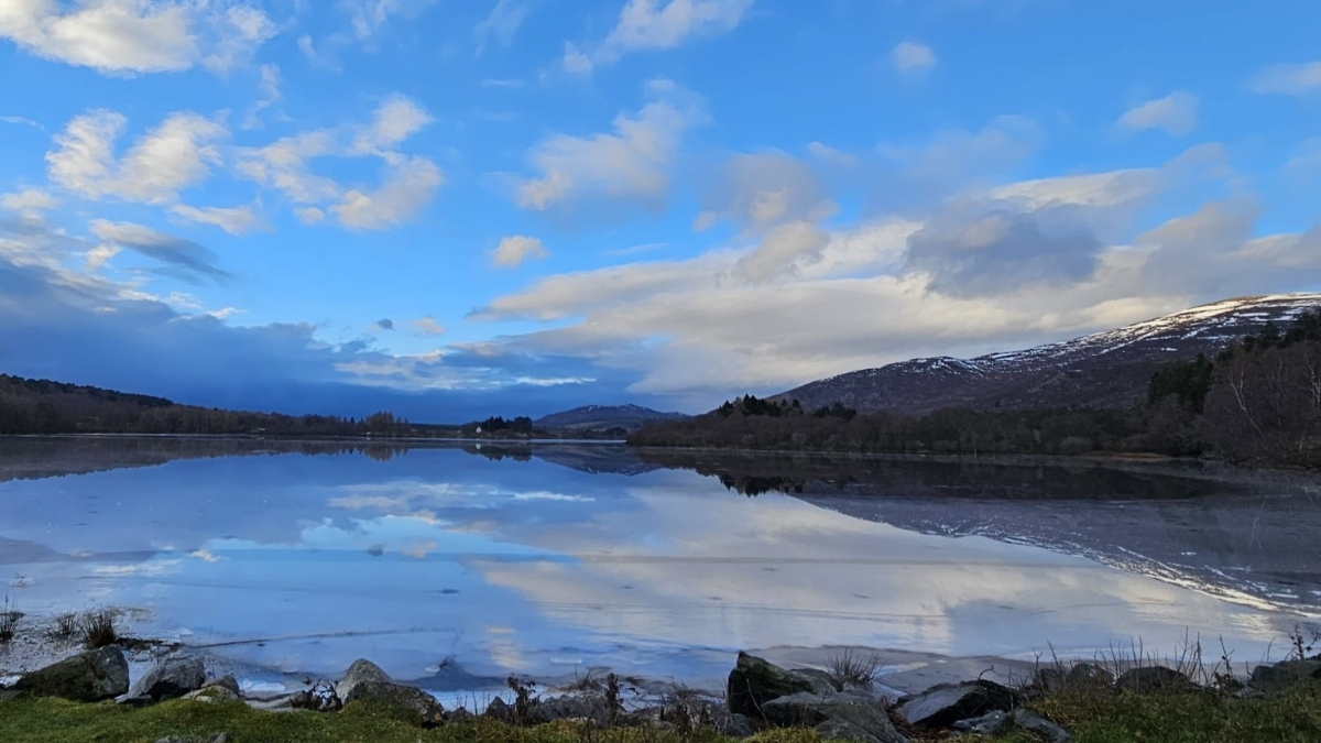 View over icy Loch Alviej with blue skies and some fluffy clouds